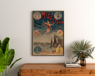 Plakat cyrkowy vintage Miss Stena, zjazd Absalona, w ramie nad drewnianą komodą, między roślinami.