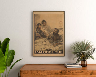 Plakat historyczny – L’Alcool tue – Eugène Burnand, oprawiony nad drewnianą komodą, między roślinami.
