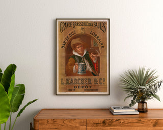 Retro plakat reklamowy Brasserie des Saules, Bar-le-Duc, oprawiony nad drewnianą komodą, między roślinami.