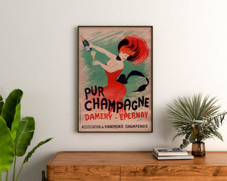 Retro plakat reklamowy Champagne Damery-Épernay, oprawiony nad drewnianą komodą, między roślinami.