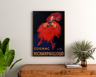 Vintage plakat reklamowy Cognac Richarpailloud, oprawiony nad drewnianą komodą, między roślinami.