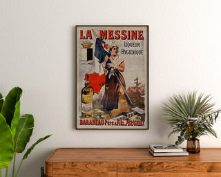 Retro plakat reklamowy La Messine, likier, oprawiony nad drewnianą komodą, między roślinami.