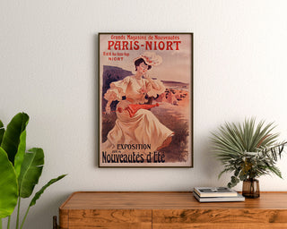 Vintage plakat reklamowy Paryż–Niort, letnie nowości, oprawiony nad drewnianą komodą między roślinami.