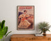 Vintage plakat reklamowy Paryż–Niort, letnie nowości, oprawiony nad drewnianą komodą między roślinami.