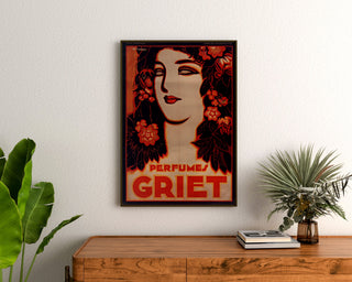 Plakat reklamowy w stylu vintage Perfumes Griet, oprawiony nad drewnianą komodą, między roślinami.