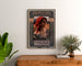 Plakat vintage Amica, opera, oprawiony nad komodą z drewna, między roślinami.