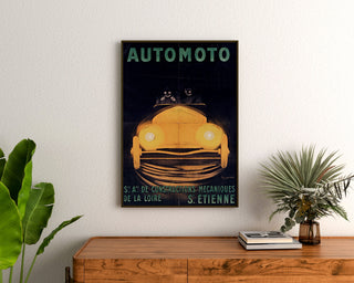Wintage plakat Automoto, Saint-Étienne, w ramie nad drewnianą komodą, między roślinami.