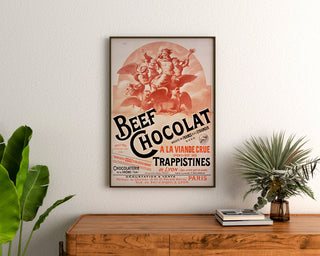 Wintage plakat Beef Chocolat, czekoladziarnia z Drôme, oprawiony nad drewnianą komodą, między roślinami.