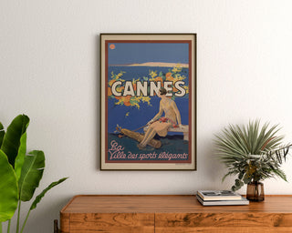 Plakat vintage Cannes, Les Sports élégants, oprawiony nad drewnianą komodą, między roślinami.