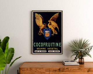 Plakat vintage Cocofruitine, masło roślinne, oprawiony nad komodą z drewna, między roślinami.