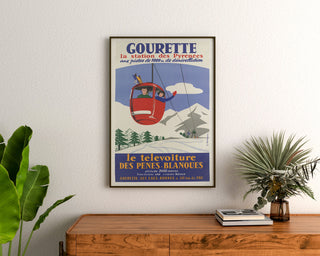 Plakat vintage Gourette, télévoiture, w ramie nad drewnianą komodą, między roślinami.