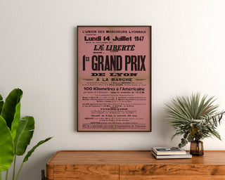 Plakat vintage Grand Prix de Lyon, marsz, oprawiony nad drewnianą komodą między roślinami.