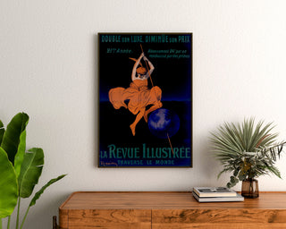 Plakat vintage La Revue illustrée, w ramie nad drewnianą komodą, między roślinami.
