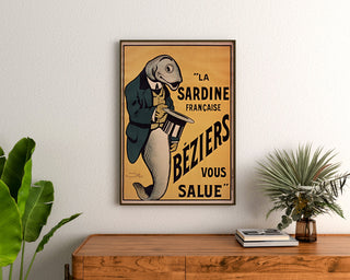 Wydruk plakatowy vintage La Sardine française, Béziers, oprawiony nad drewnianą komodą, między roślinami.