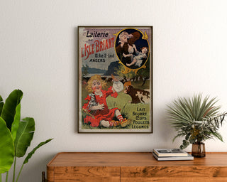 Plakat vintage Laiterie de l’Isle Briant, Angers, w ramie nad drewnianą komodą, między roślinami.