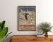Plakat vintage Les Eaux-Bonnes, sporty zimowe, oprawiony nad drewnianą komodą, między roślinami.