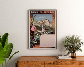 Plakat vintage Lourdes, chemins de fer du Midi, w ramie nad drewnianą komodą, między roślinami.