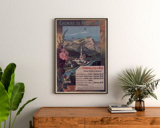 Plakat vintage Lourdes, kurorty nadmorskie, oprawiony nad drewnianą komodą między roślinami.