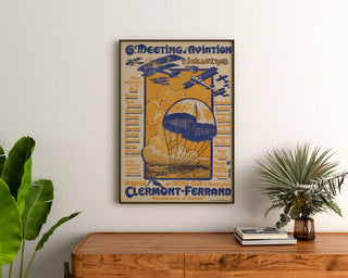 Plakat vintage Meeting d’aviation, Clermont-Ferrand, oprawiony nad drewnianą komodą, między roślinami.