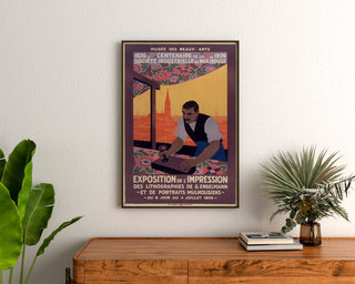 Plakat vintage Mulhouse, wystawa litograficzna, oprawiony nad drewnianą komodą między roślinami.