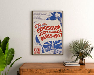 Plakat vintage Paryż 1937, wystawa międzynarodowa, oprawiony nad drewnianą komodą, między roślinami.