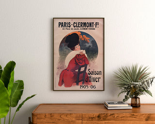 Plakat vintage Paris-Clermont, sezon zimowy, oprawiony nad drewnianą komodą, między roślinami.