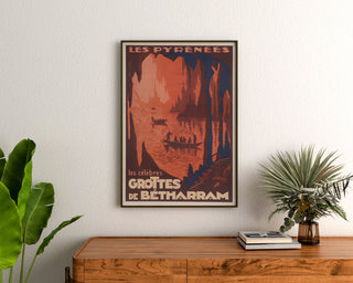 Plakat vintage Pireneje, Grottes de Bétharram, w ramie nad drewnianą komodą, między roślinami.