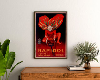 Wintage plakat Rapidol, oprawiony nad drewnianą komodą, między roślinami.