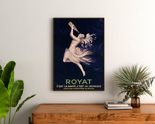 Plakat vintage Royat, zdrowie i młodość, w ramie nad drewnianą komodą, między roślinami.