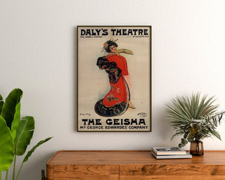 Plakat vintage The Geisha, Daly’s Theatre, oprawiony nad drewnianą komodą, między roślinami.