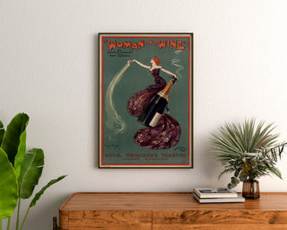 Plakat vintage Woman and Wine, Princess’s Theatre, oprawiony nad drewnianą komodą, między roślinami.